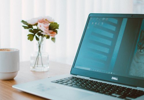 Black and Gray Dell Laptop Beside White Ceramic Mug