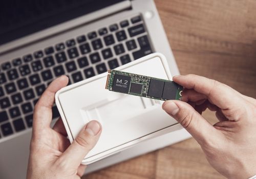 Man unpacks the newly purchased M.2 SSD drive over his desk with a modern laptop