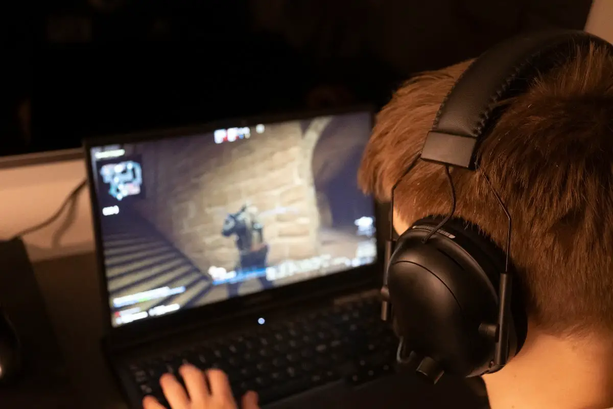 Person Wearing Headphones Playing Online Games on Laptop