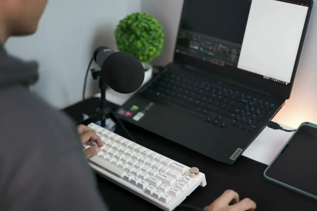 Man Sitting Front of His Desk with a Laptop, Keyboard and a Microphone